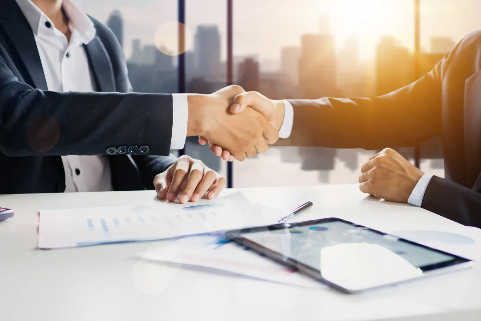 Two professionals shaking hands across a meeting table in a bright office