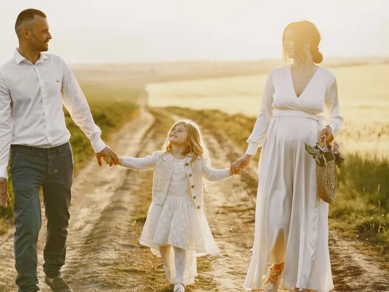 Parents walking hand in hand with their daughter down a country path