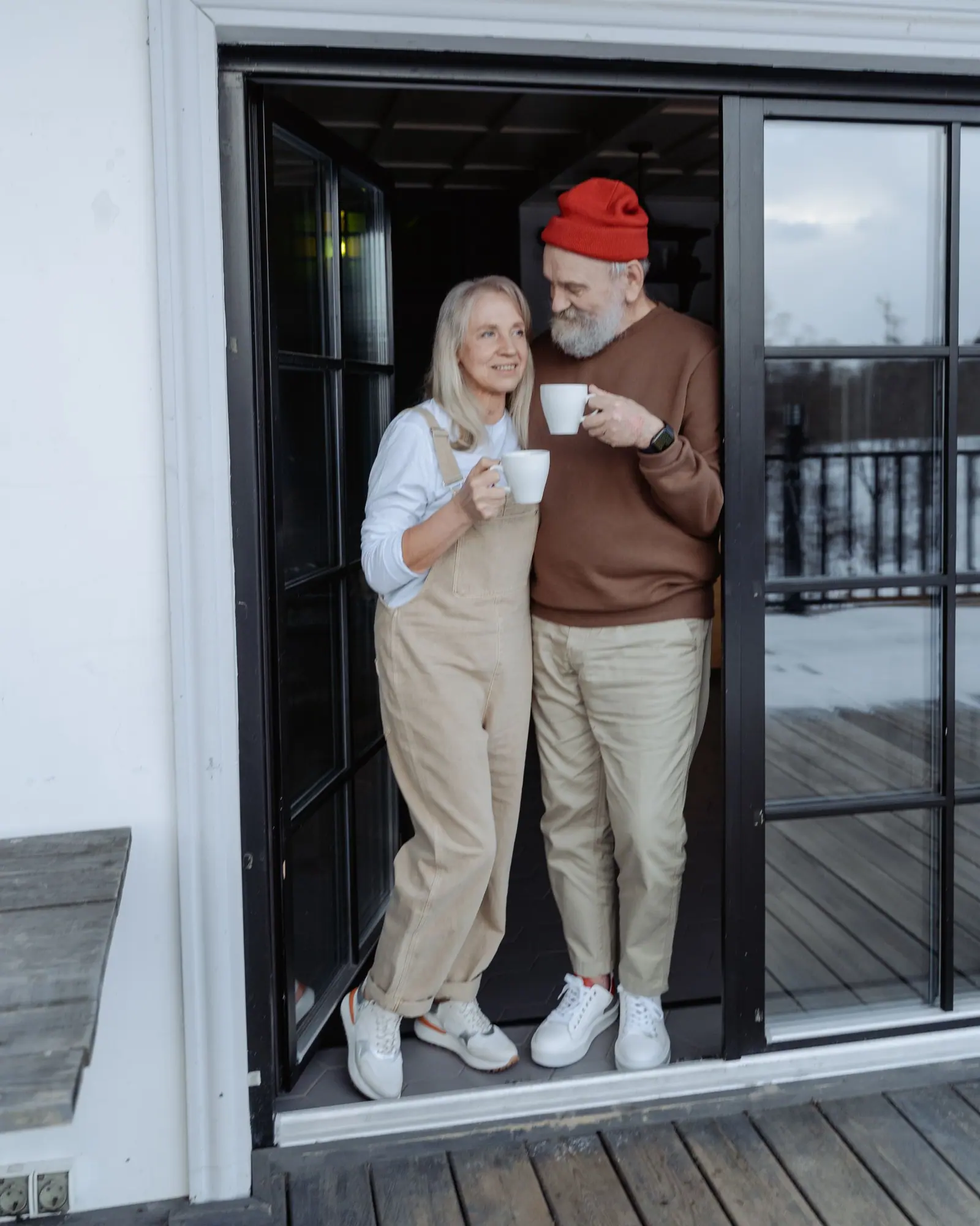 An older couple standing together with coffee at the door of their home